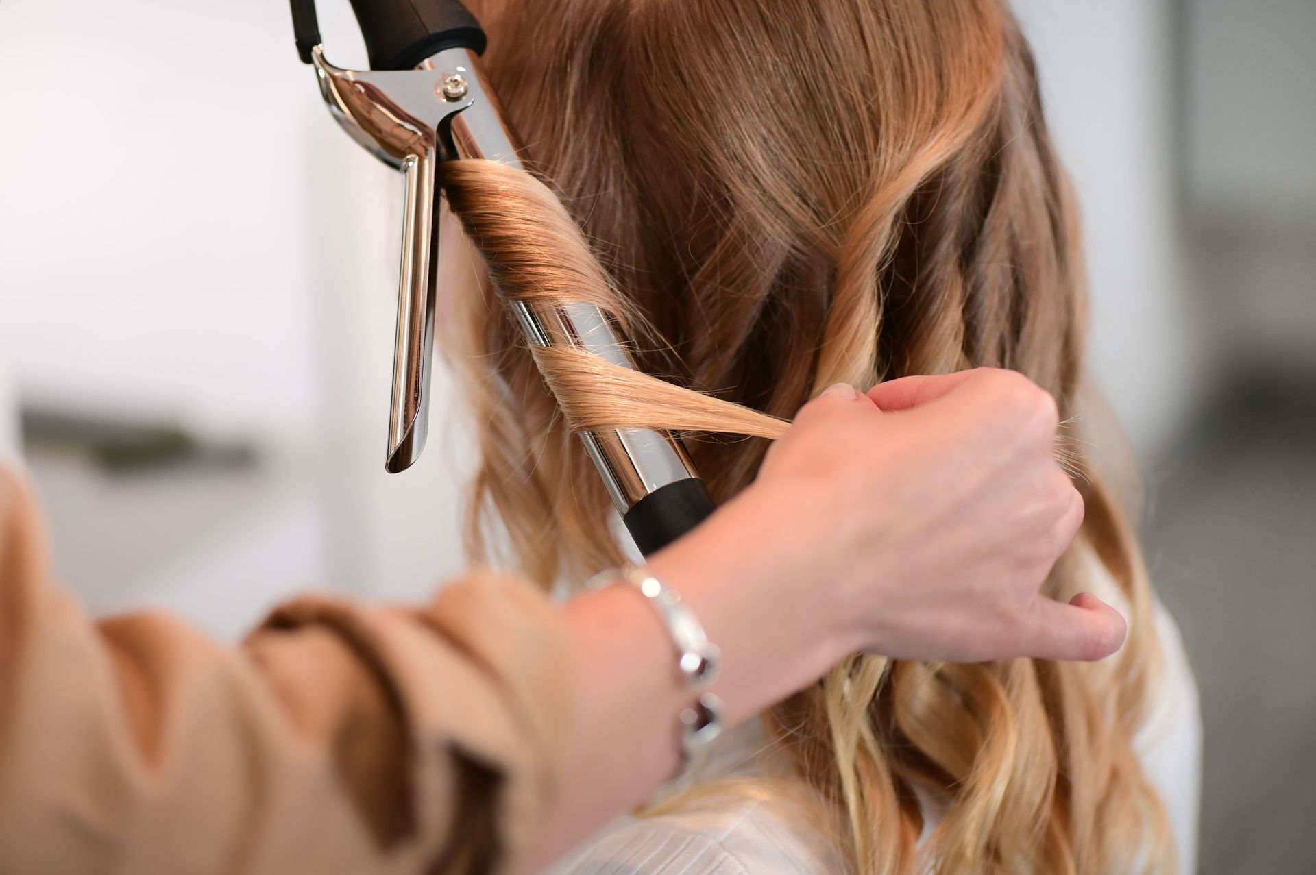 Person curling hair with a curling iron; blonde hair, close-up shot, indoors.