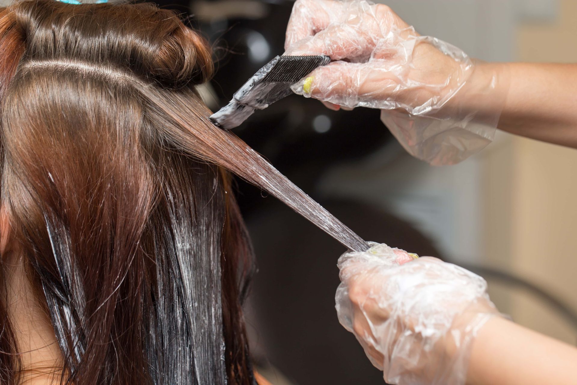 Hands in gloves applying hair dye to a person's hair, in a salon.