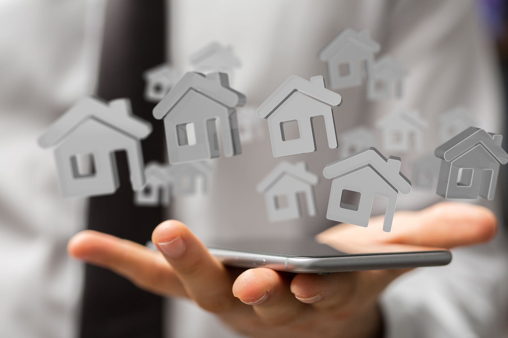 A close-up of a hand holding a cellphone with pop-ups of various grey-colored home emojis. A close-up of a hand holding a cellphone with pop-ups of various grey-colored home emojis.