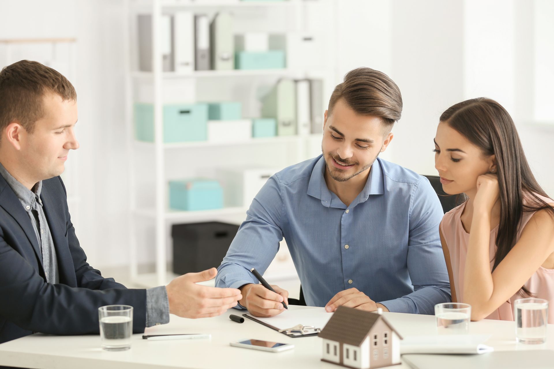 A couple signs papers with an agent for low home loan mortgage rates in a bright office. A couple signs papers with an agent for low home loan mortgage rates in a bright office.