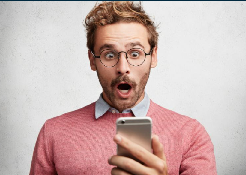 man looking at phone shocked he did not get the job he wanted