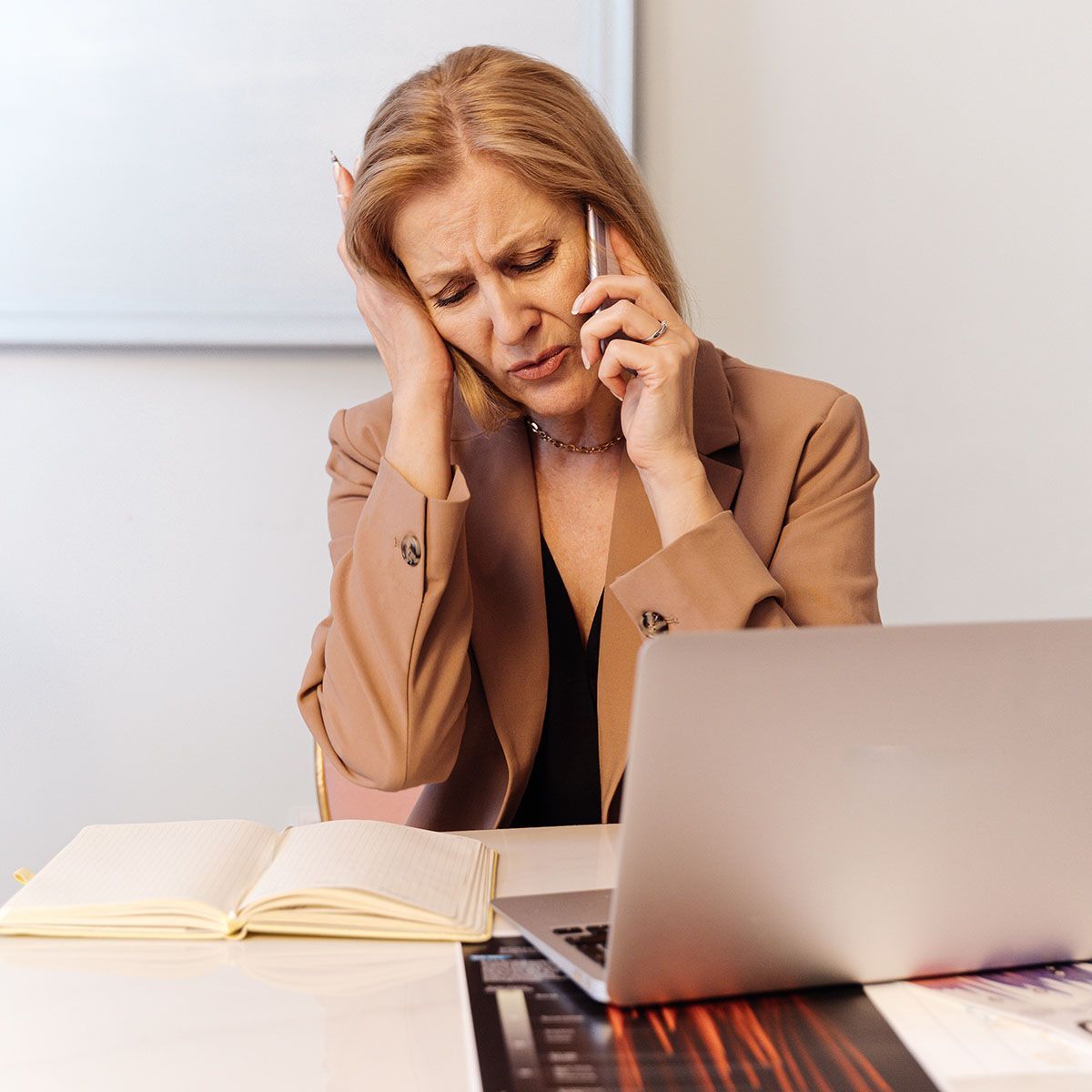 professionally dressed woman looking tired while talking on the phone at a desk