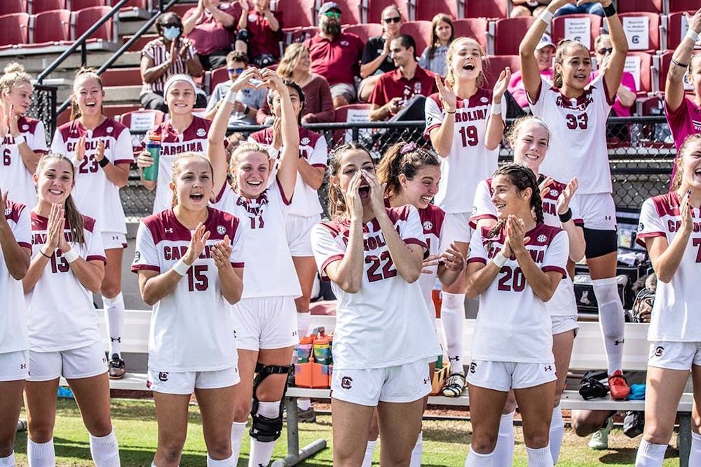 A group of female soccer players are standing on a field with their hands in the air.