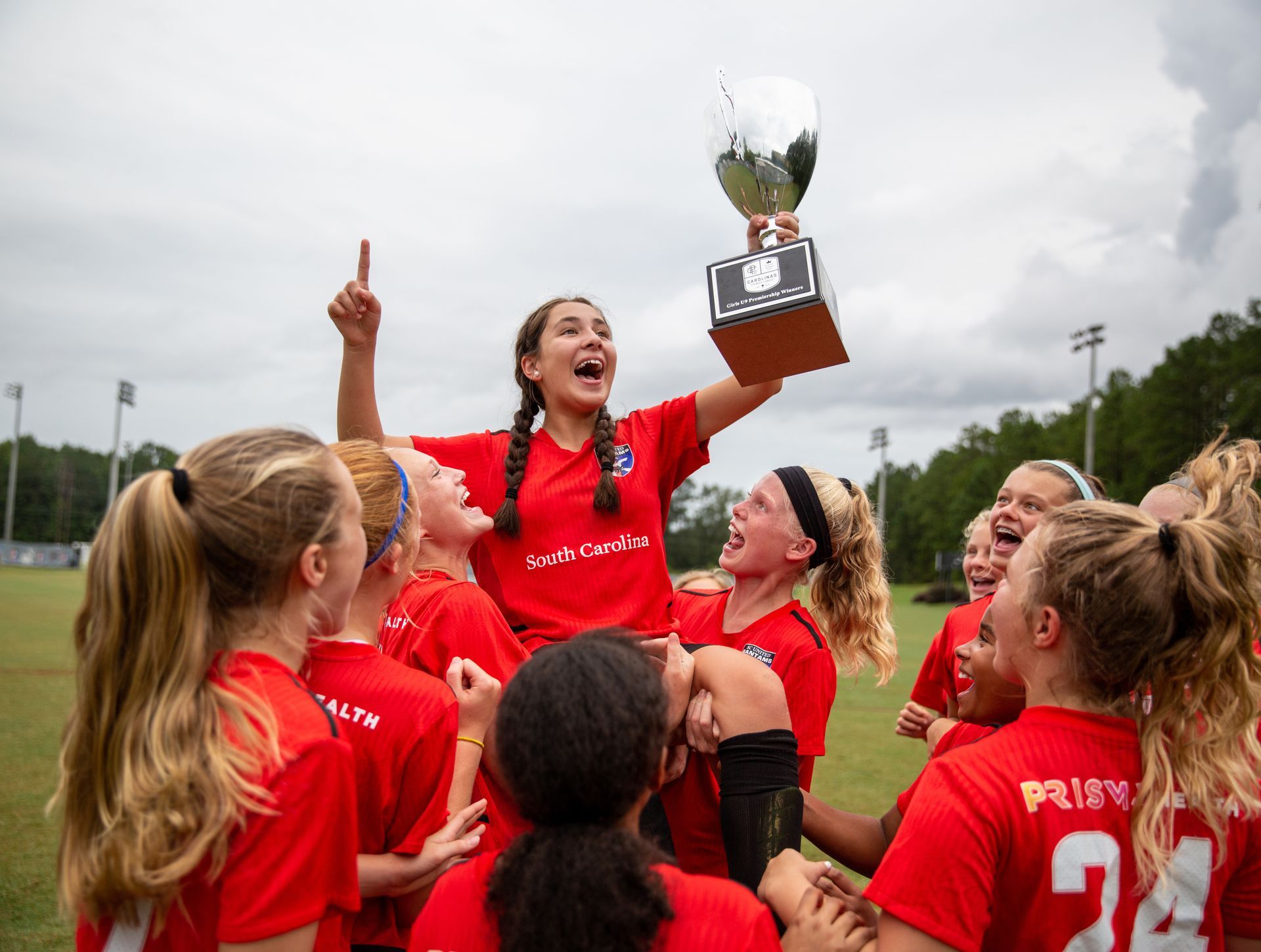 A group of young South Carolina United FC girls are holding a trophy in the air.