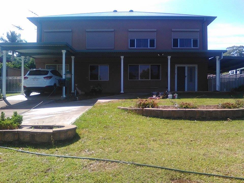 A car is parked under a canopy in front of a house.