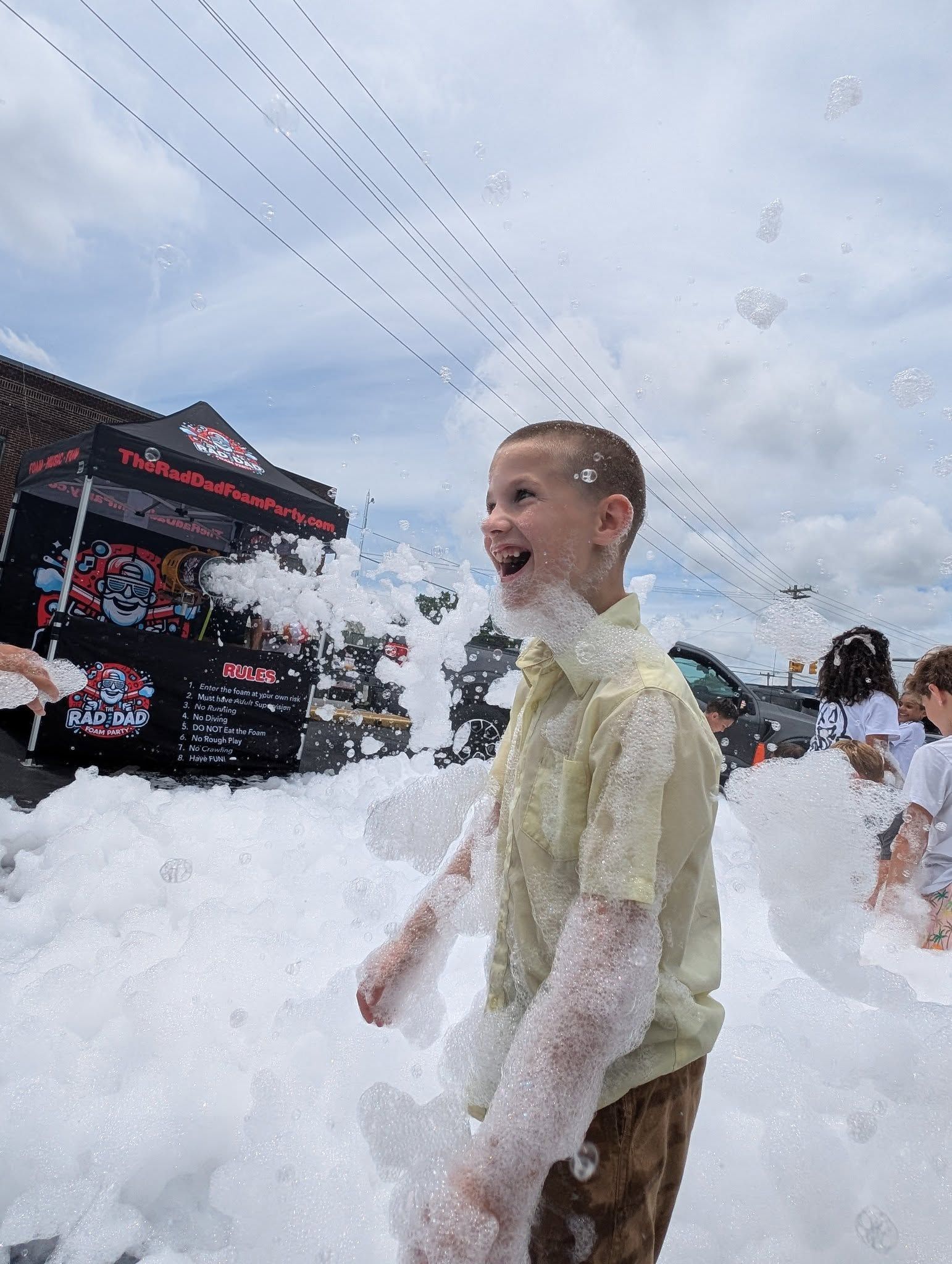 Person smiling in a foam-filled outdoor scene near a black-and-red tent