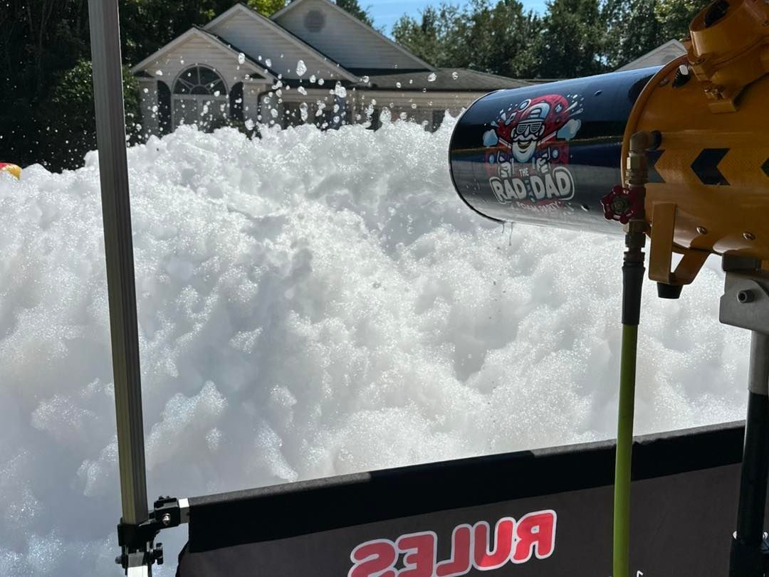 Foamy water spraying from a RYOBI pressure washer toward a house driveway in a residential yard