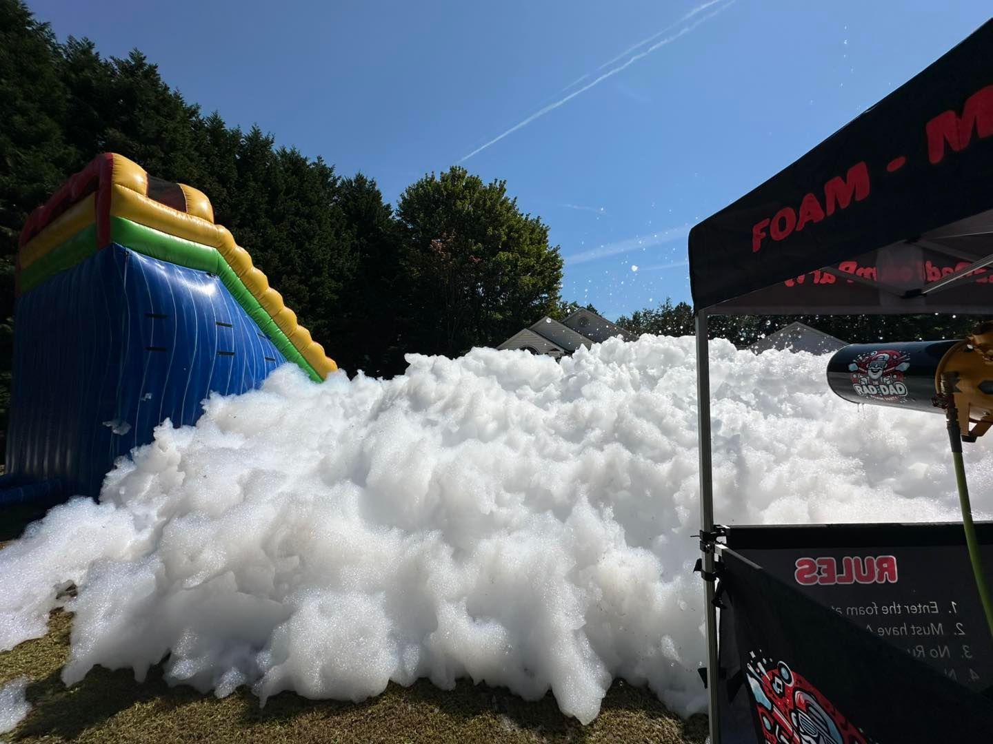Foam-covered outdoor play area beside a blue-and-yellow inflatable slide under a canopy