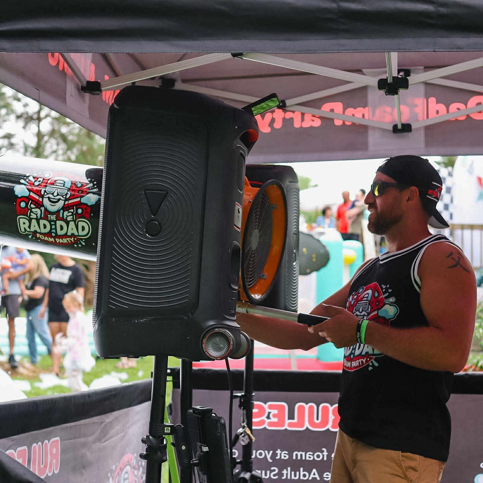 Woman in black sportswear setting up a large speaker under a tent at an outdoor event