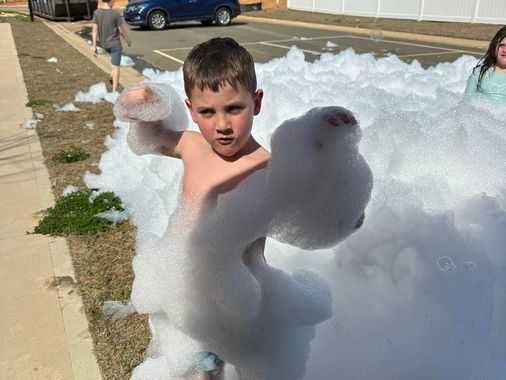 Child playing in a large pile of white foam outdoors, reaching toward the camera.