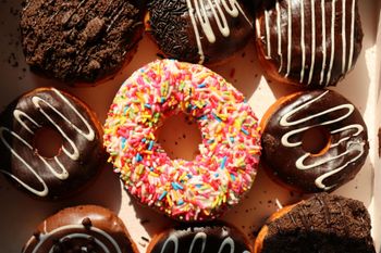Assorted chocolate and sprinkled donuts, with a pink sprinkled donut centered on a warm brown background