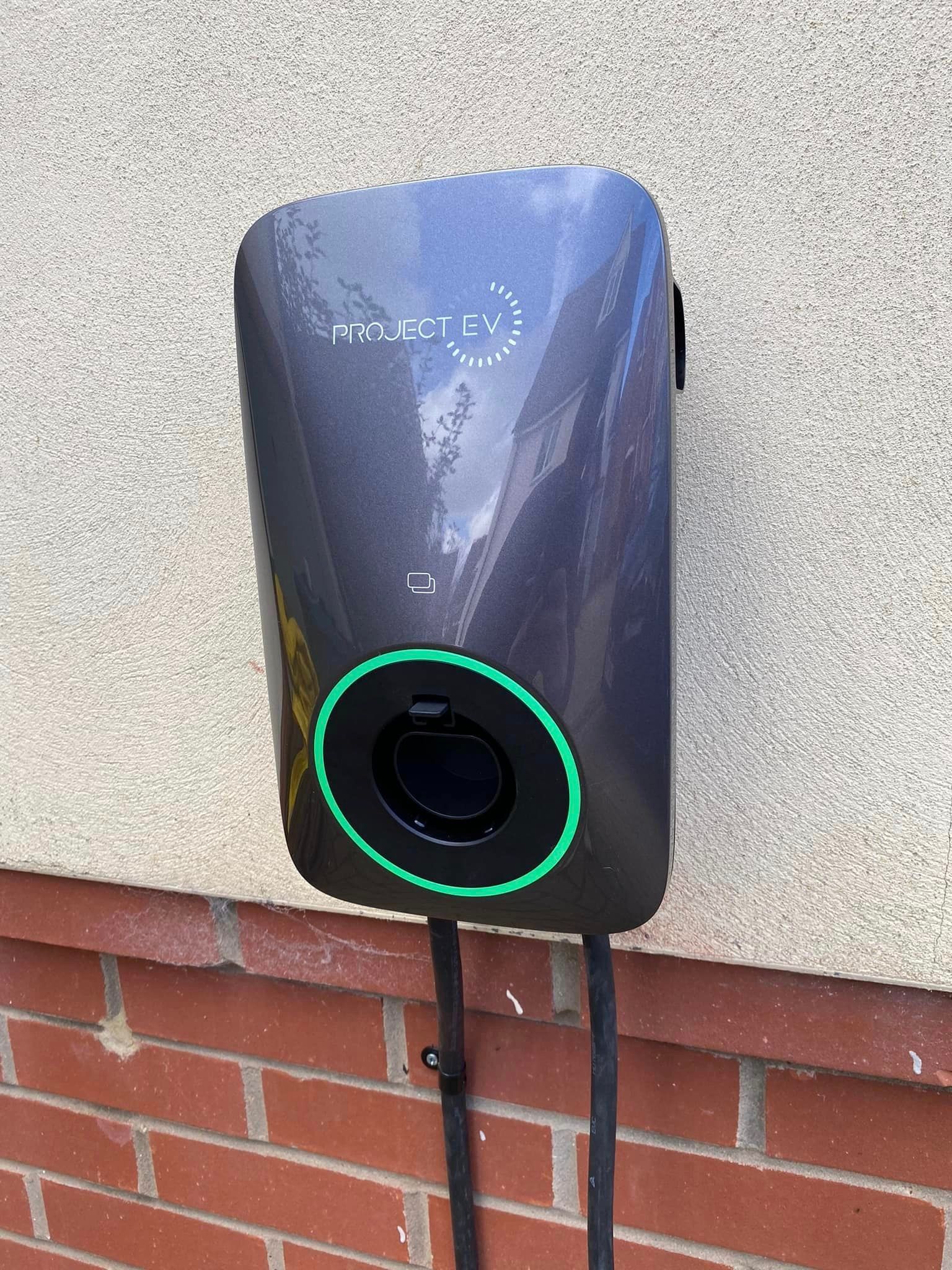 A gray electric car charger is attached to a brick wall.