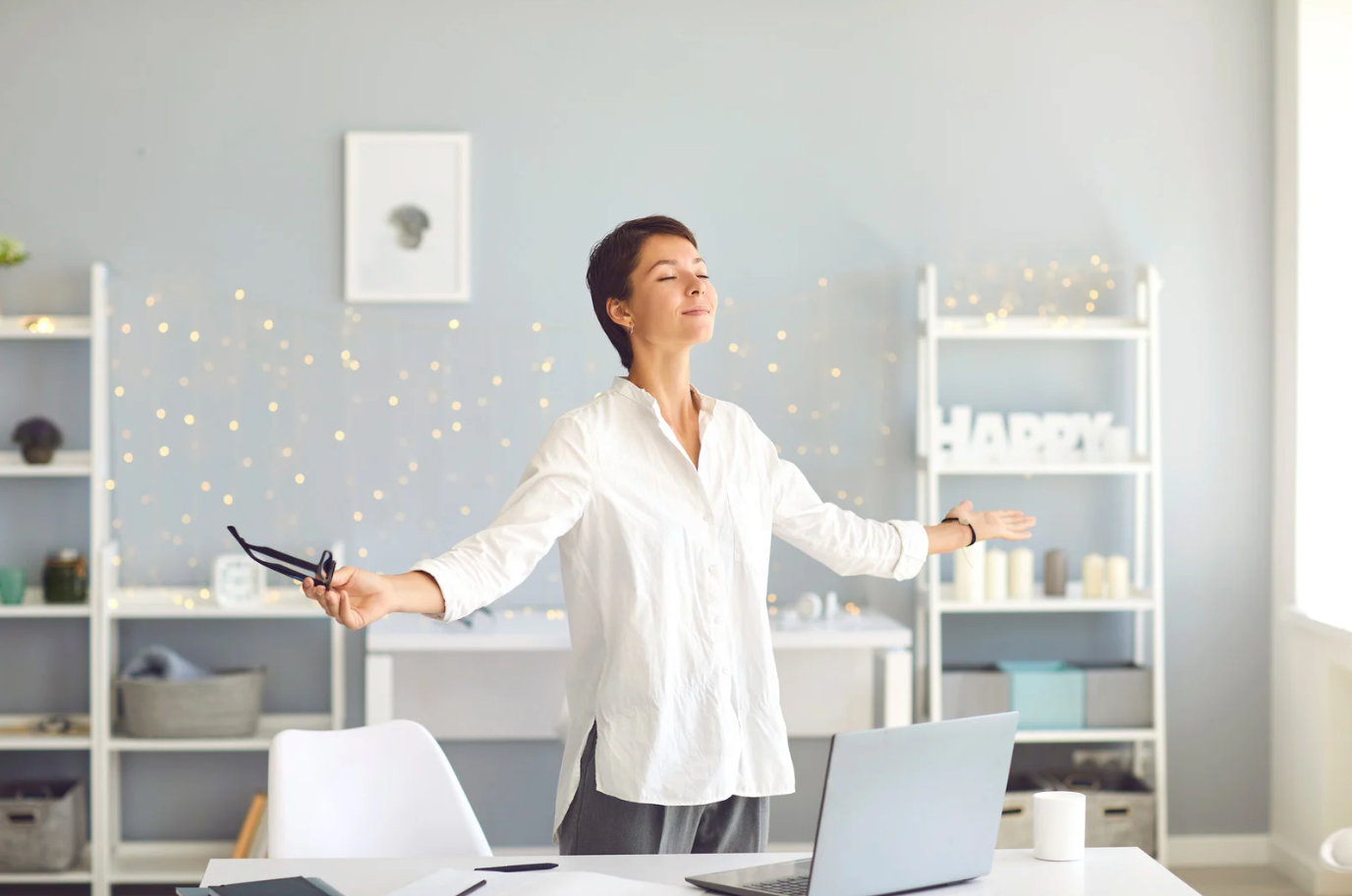 A woman is standing in front of a desk with her arms outstretched in an office.