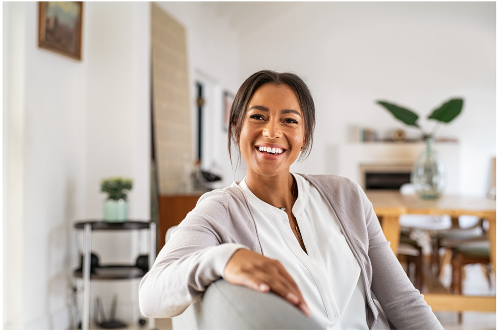 A woman is smiling while sitting in a chair in a living room.