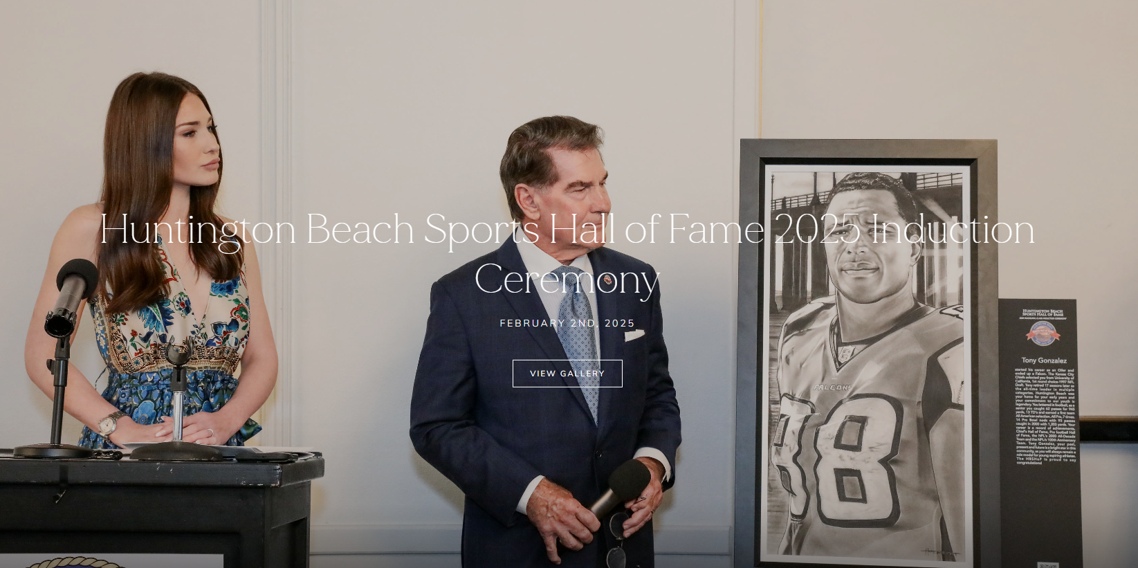 A man and a woman stand by a podium. A framed portrait of a football player hangs on the wall.