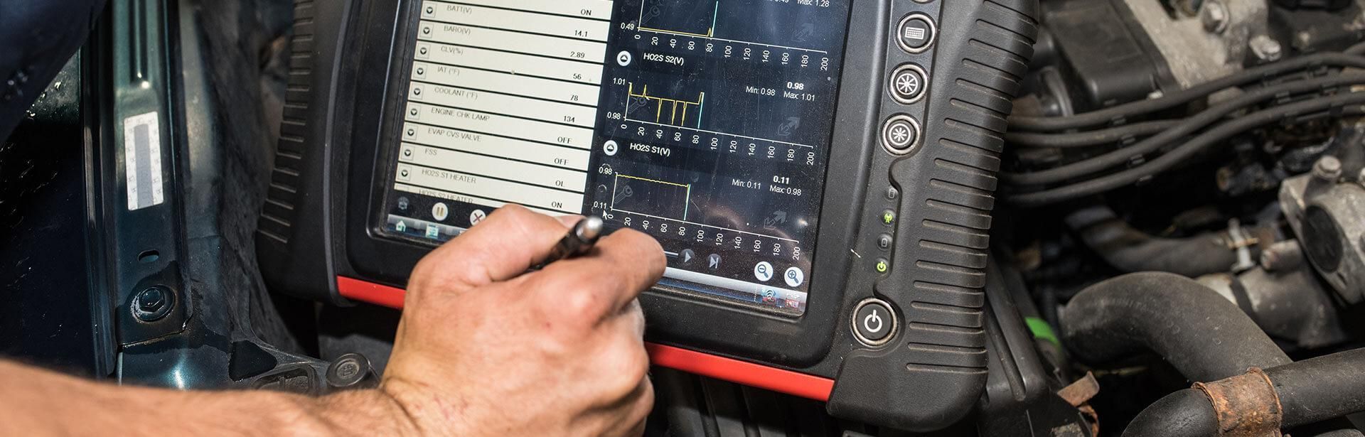 A man is using a computer to check the engine of a car | Nealey Tire & Auto