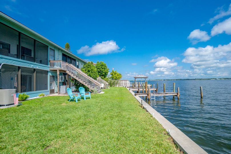 A house with a dock and chairs next to a body of water.