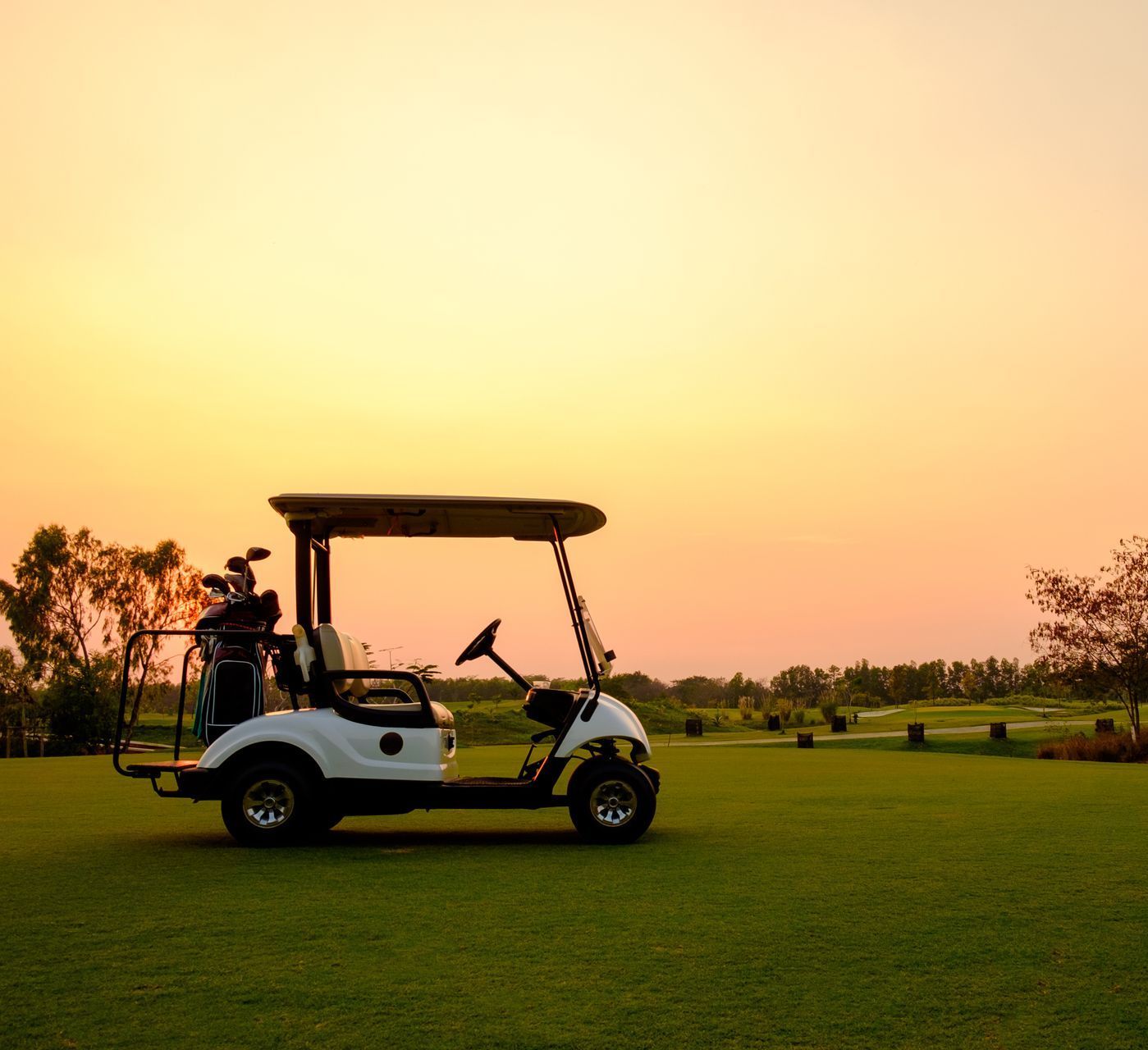 A golf cart is parked in a grassy field at sunset