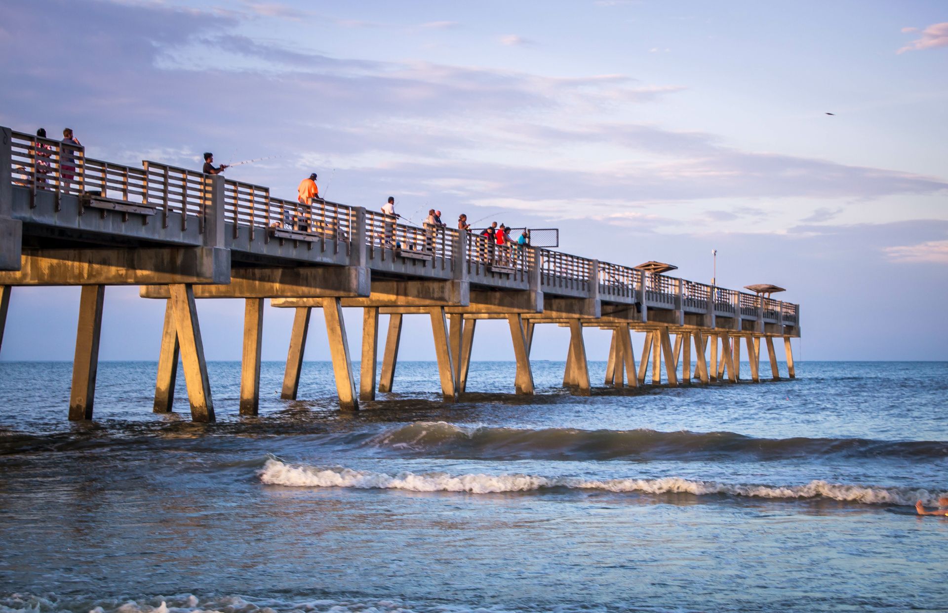 People are fishing on a pier in the ocean.