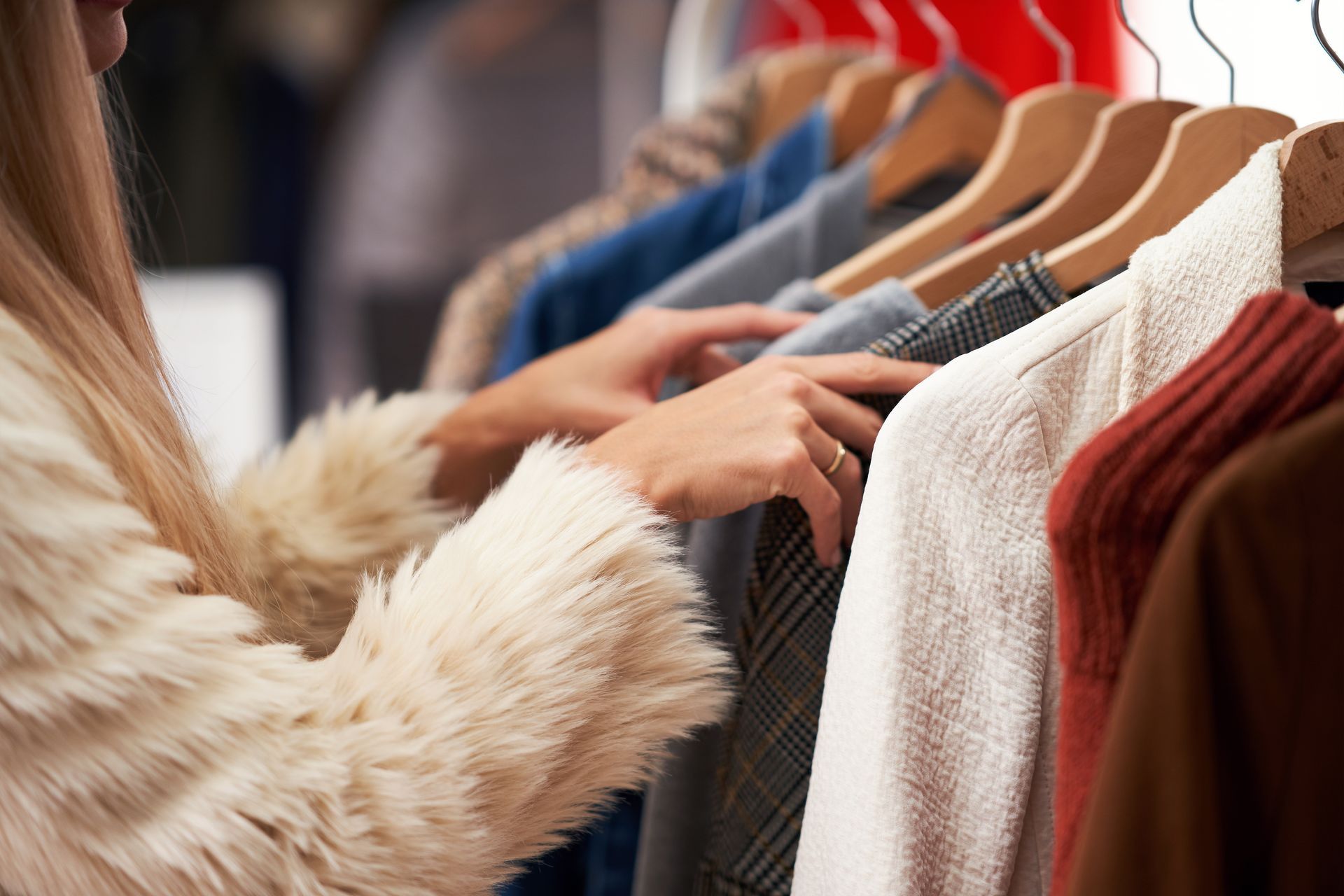A woman in a fur coat is looking at clothes in a closet.