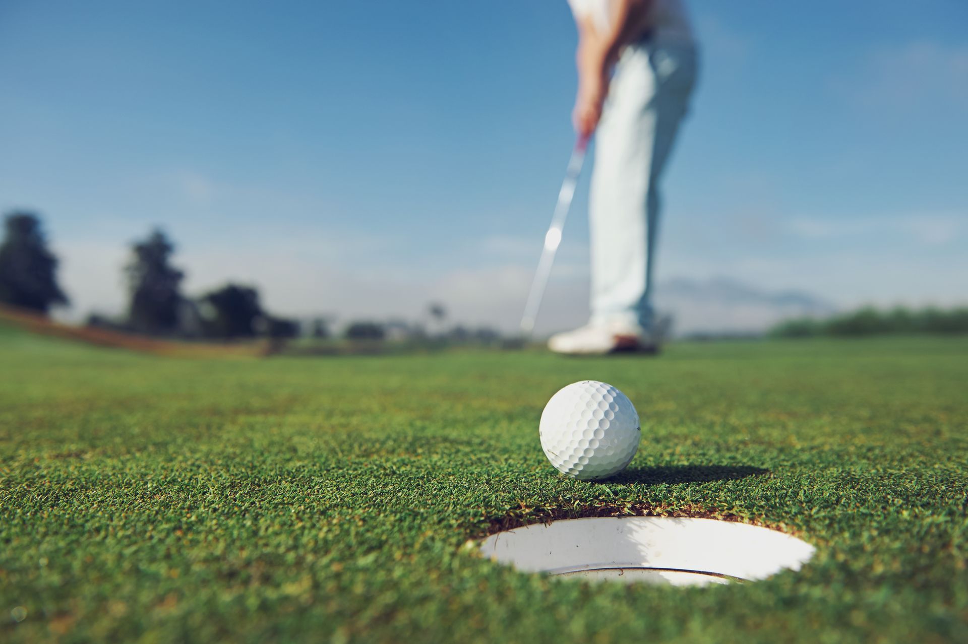 A golfer is putting a golf ball into a hole on a golf course.