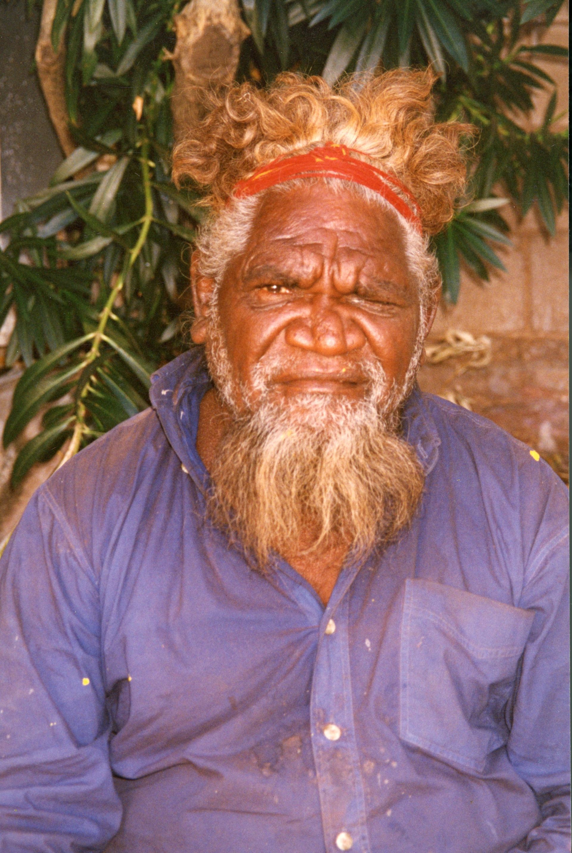 A man with a beard and a crown on his head is wearing a blue shirt.