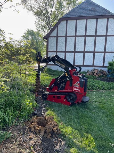 A red tractor is digging a hole in the ground in front of a house.