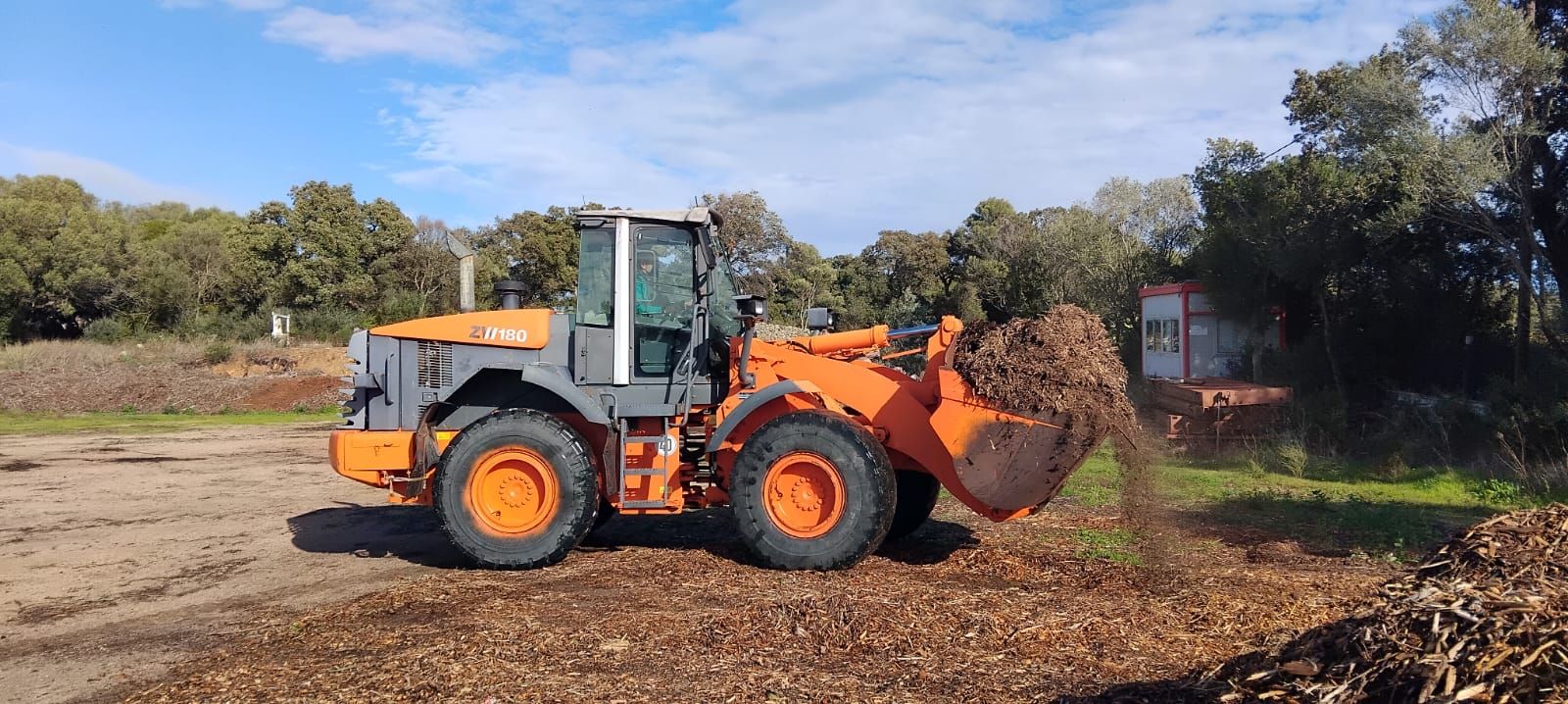 Una pala caricatrice frontale arancione e grigia sposta trucioli di legno in una giornata di sole.