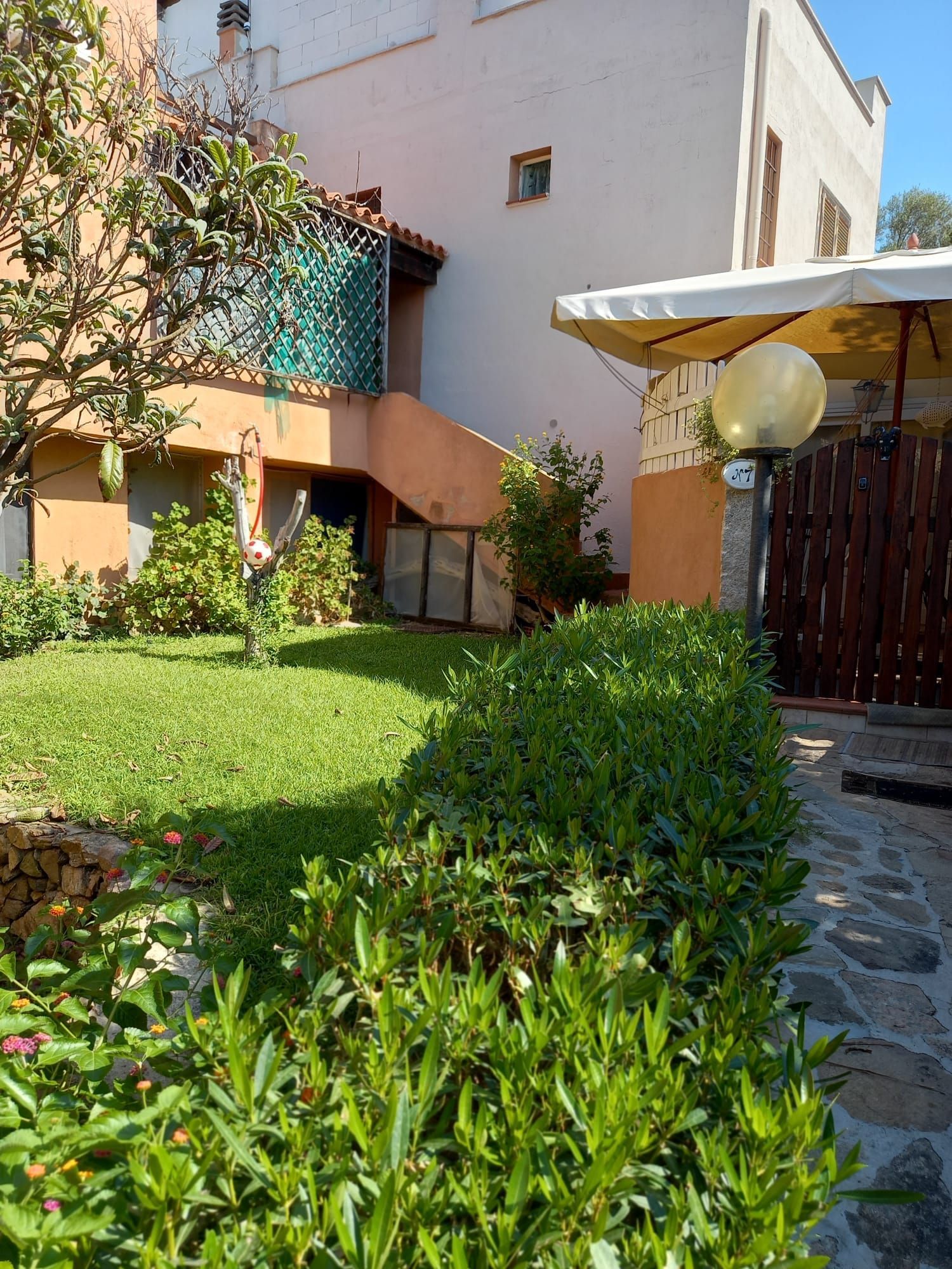 Giardino rigoglioso di fronte a un edificio dai colori chiari. Ambiente esterno soleggiato con scale e un piccolo cancello.