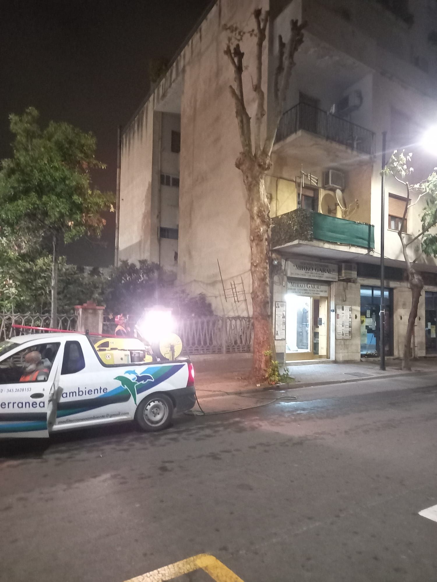 Camion parcheggiato in strada, che spruzza. Edificio e albero sullo sfondo di notte.