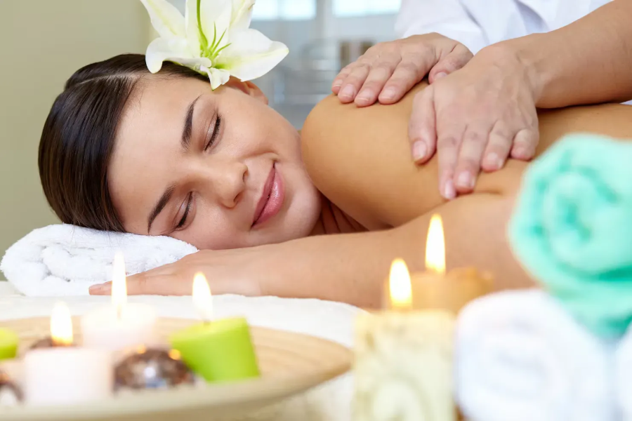 Woman receiving a spa massage with candles and rolled towels nearby