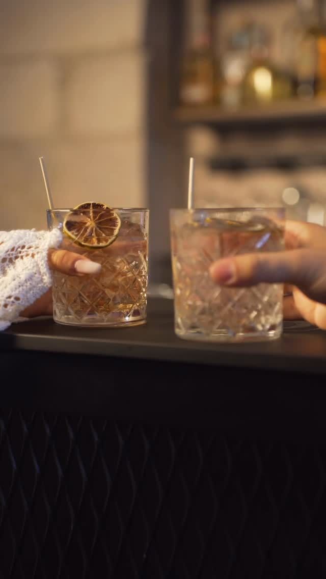 Una coppia si siede in un bar sul lungomare e sorseggia un drink, ammirando il lago e le montagne al tramonto.