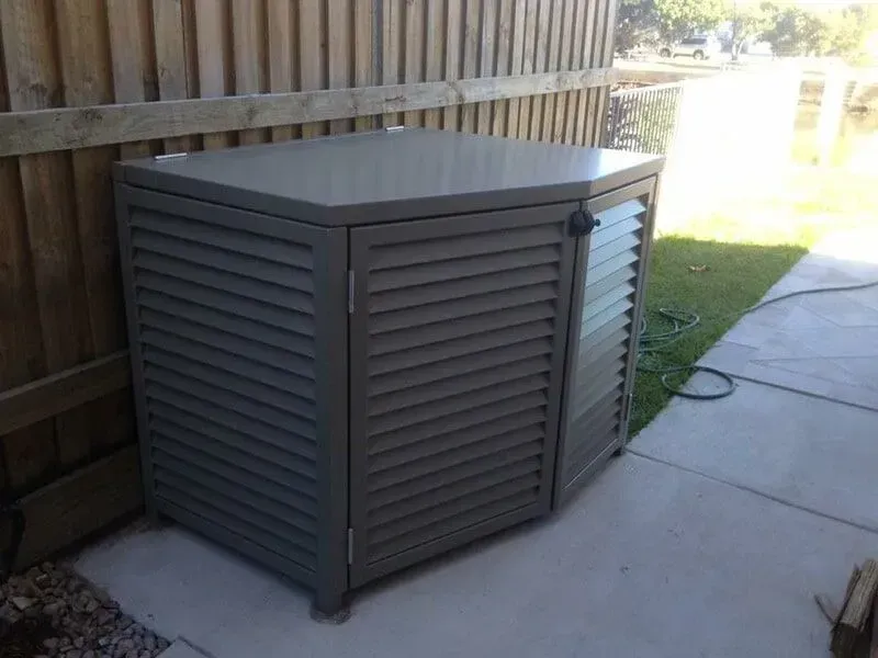 A gray metal box with shutters on the doors is sitting on a sidewalk next to a wooden fence. — Sunshine Gates in Kunda Park, QLD