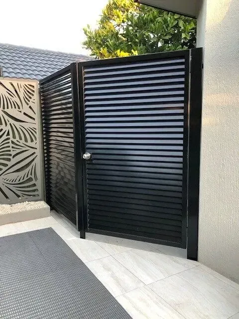 A black gate with shutters on it is sitting next to a wall. — Sunshine Gates in Kunda Park, QLD