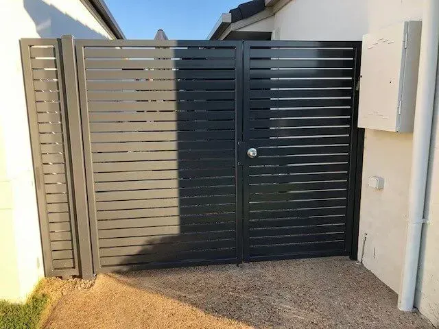 A black fence with a door is next to a house. — Sunshine Gates in Kunda Park, QLD