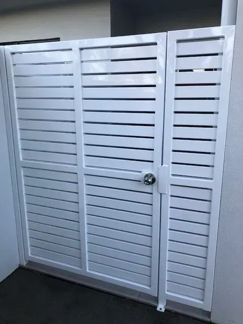A white gate with a door is sitting next to a wall. — Sunshine Gates in Kunda Park, QLD