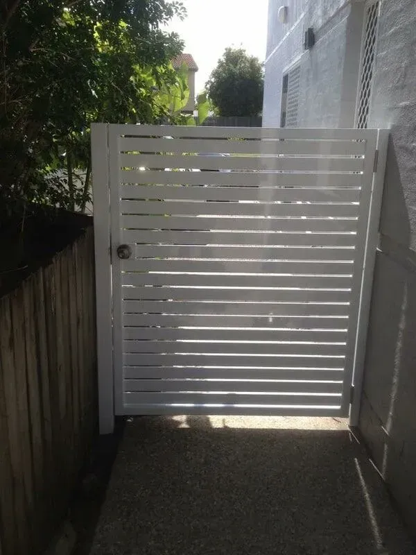 A white gate with a wooden fence behind it.— Sunshine Gates in Kunda Park, QLD