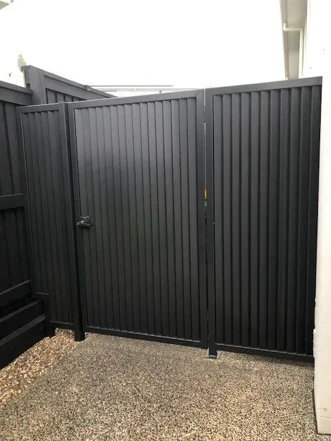 A black gate is sitting next to a black fence.— Sunshine Gates in Kunda Park, QLD