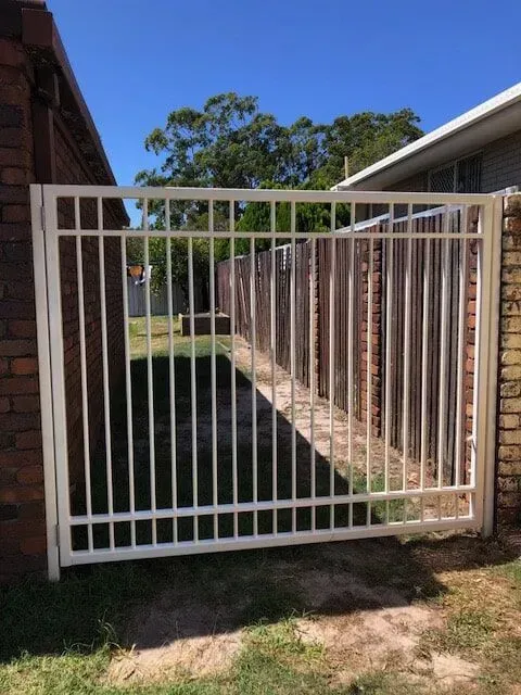 A white gate is sitting next to a brick wall. — Sunshine Gates in Kunda Park, QLD