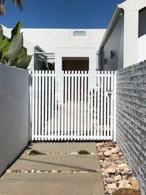 A white fence surrounds the entrance to a house. — Sunshine Gates in Kunda Park, QLD