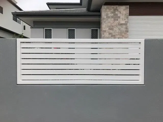 A white fence is sitting on top of a gray wall in front of a house. — Sunshine Gates in Kunda Park, QLD
