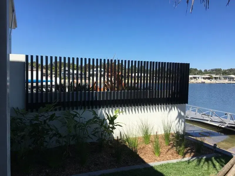 A black fence surrounds a yard with a view of a body of water. — Sunshine Gates in Kunda Park, QLD