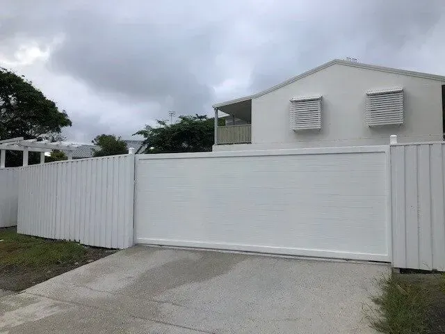 A white fence surrounds a white house with a sliding gate. — Sunshine Gates in Kunda Park, QLD