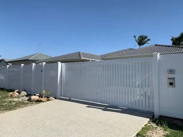 A white fence is surrounding a house with a sliding gate. — Sunshine Gates in Kunda Park, QLD