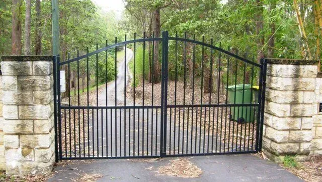 A black wrought iron gate is open to a driveway surrounded by trees. — Sunshine Gates in Kunda Park, QLD