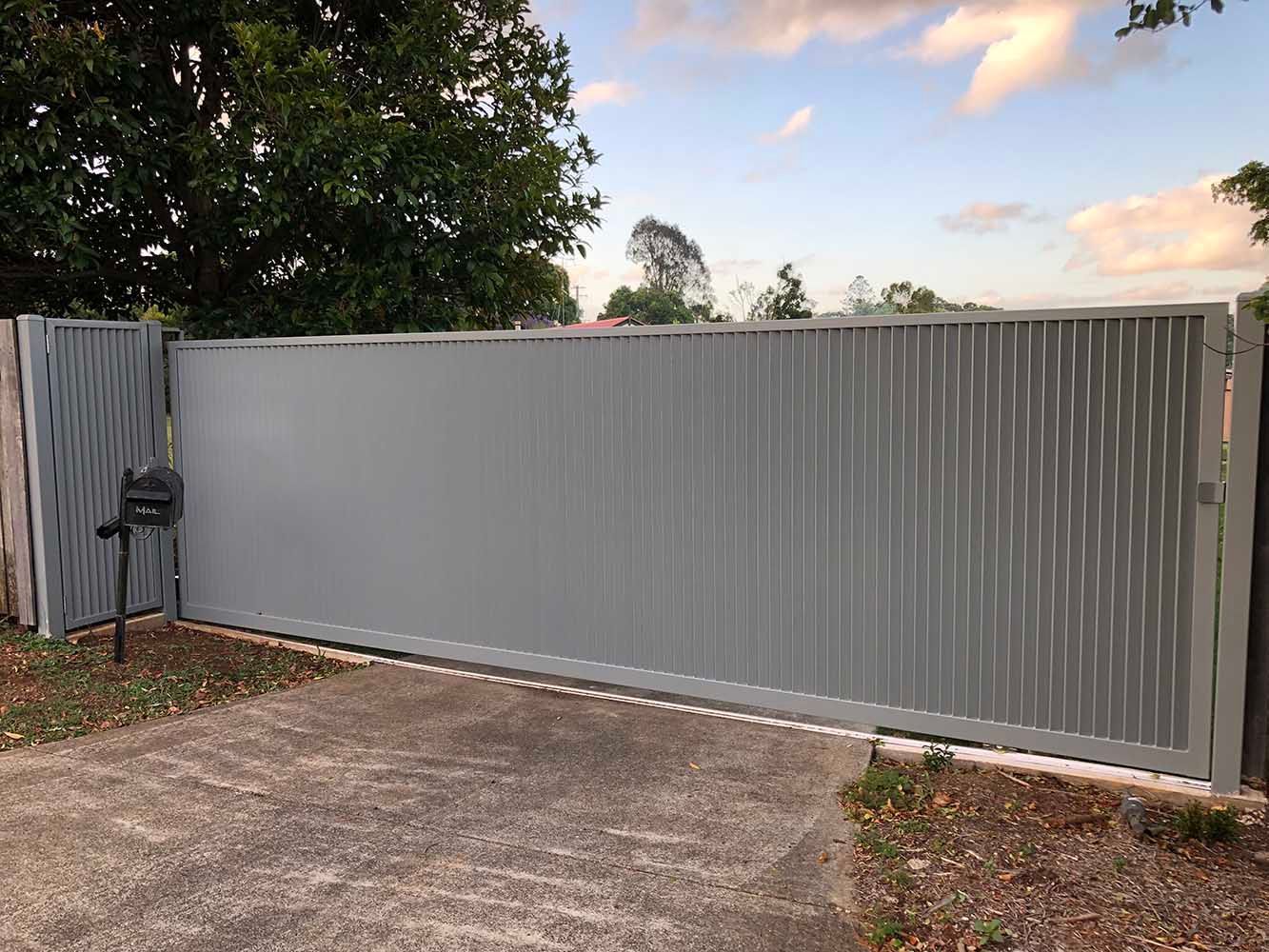 A gray sliding gate is sitting on top of a concrete driveway next to a mailbox. — Sunshine Gates in Kunda Park, QLD