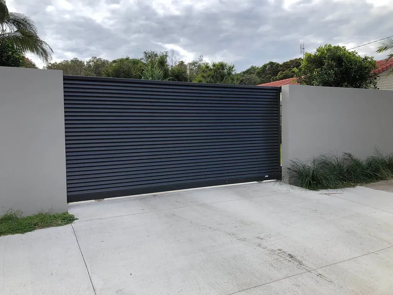 A black garage door is sitting next to a white wall. — Sunshine Gates in Kunda Park, QLD