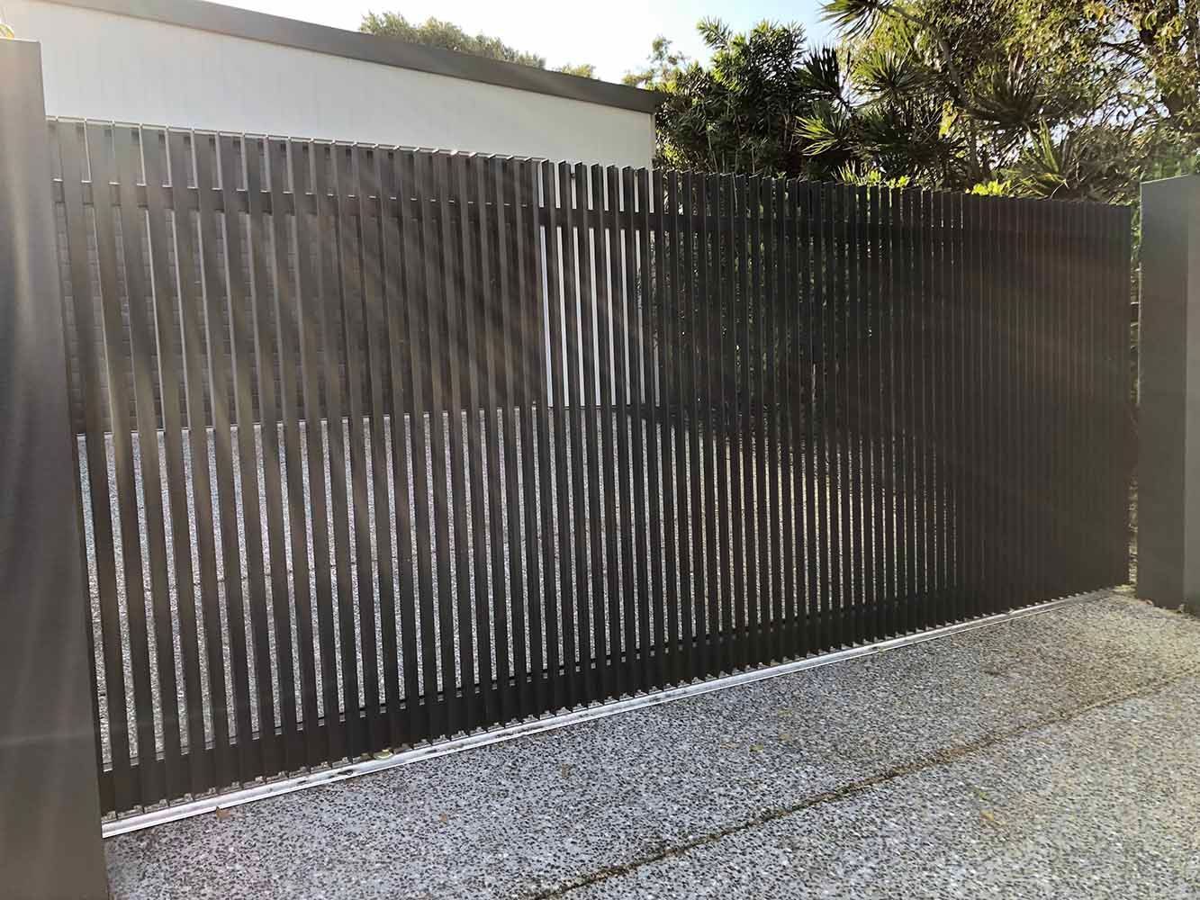 A black sliding gate is sitting on top of a gravel driveway. — Sunshine Gates in Kunda Park, QLD