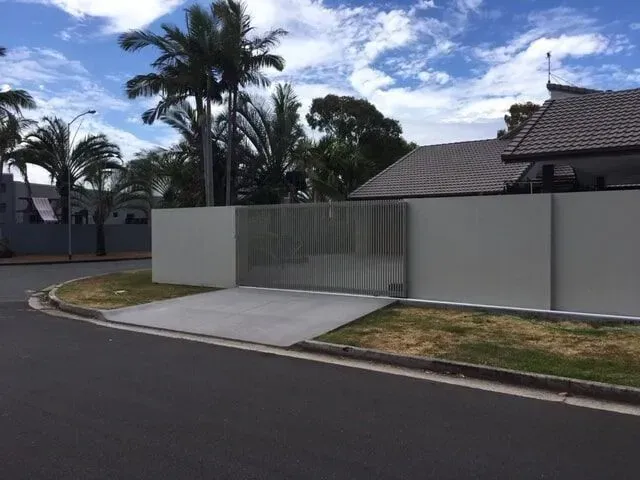 A white fence surrounds a house with palm trees in the background. — Sunshine Gates in Kunda Park, QLD