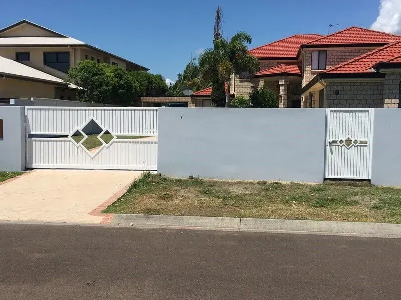 A white fence with a sliding gate in front of a house